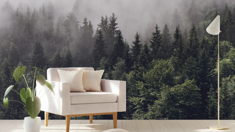 A small white loveseat and white standing lamp before a wall with forest scenic wallpaper