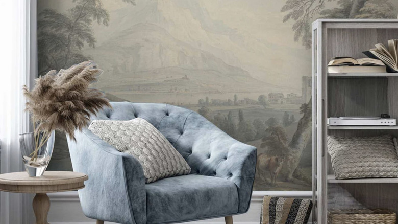 Pastoral scenic wallpaper accent wall decorated with a blue statement chair and wood side table.