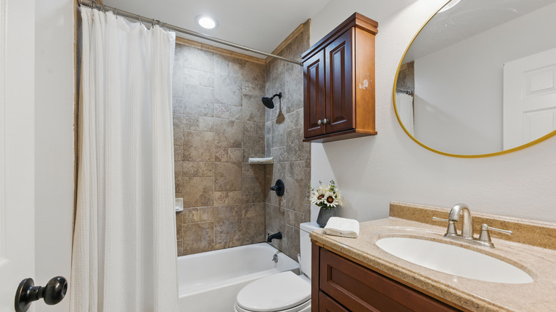 A small bathroom with cloth shower curtain and tiled tub with traditional vanity