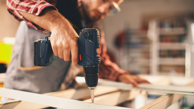 Person wearing protective goggles and drilling wood in a workshop area