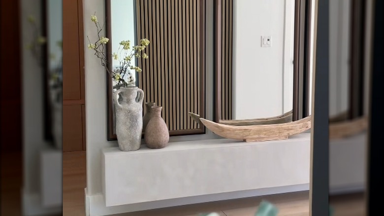 Plaster-covered floating hearth in entryway topped with two vases and a wooden piece