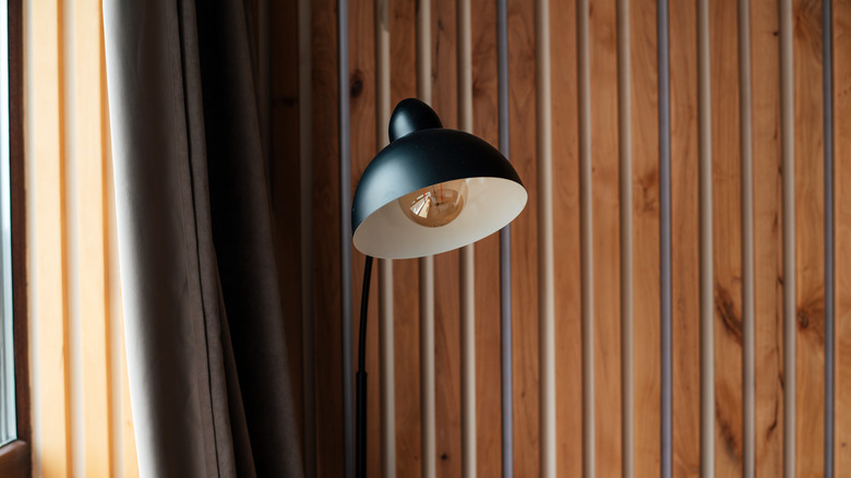 Black floor lamp against wood paneled wall