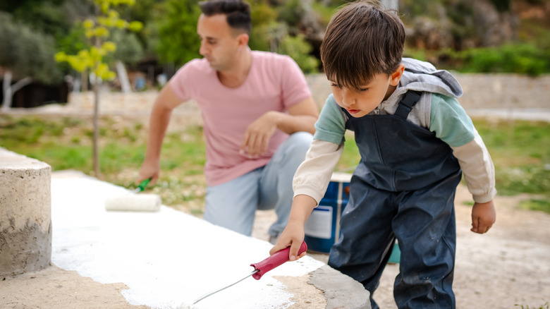 Father and son painting concrete steps in white.