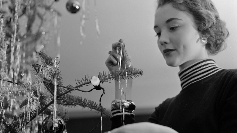 woman in 1950's decorating tree with tinsel and lights in black and white photo