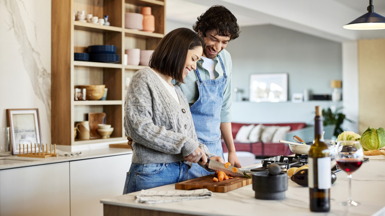 A couple stands in a modern kitchen smiling as they cook together