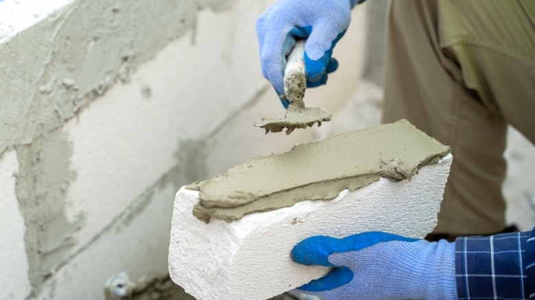 Person putting surface bonding cement on brick while building cinder block wall