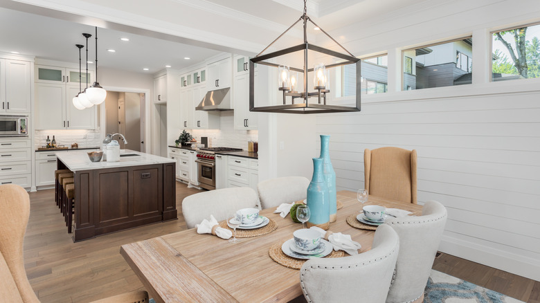 A dining room with a box lighting fixture that follows through to a kitchen with pendant lights