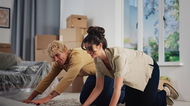 A couple rolling out a rug in a home with boxes