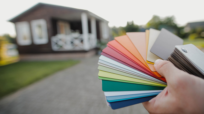 A close-up of color swatches in a person's hand with a blurred house in the background
