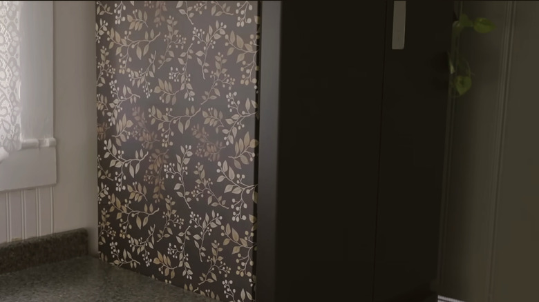 The side of a fridge with floral wallpaper.