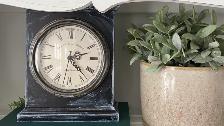 A distressed vintage clock next to a potted plant.