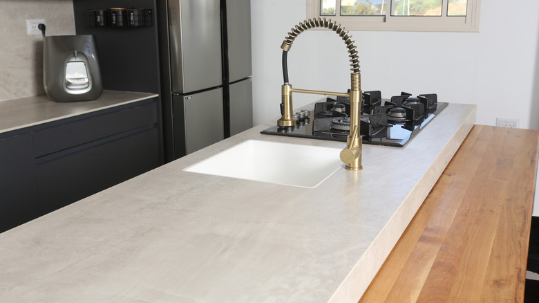 A modern kitchen with a honed countertop in a large island that also houses a cooktop, sink and brass-toned faucet
