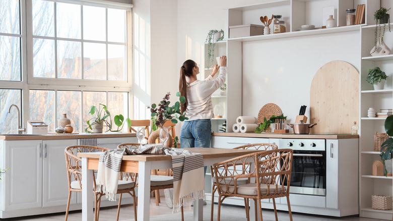 Woman adding decorative bowl to shelf on kitchen wall