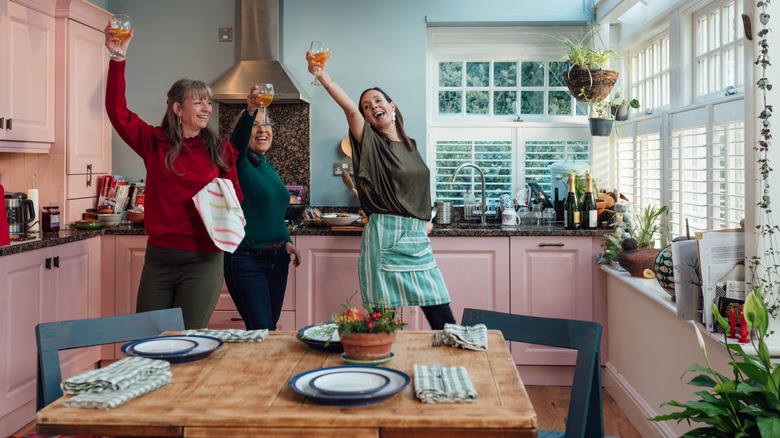 Three women celebrating with glasses raised in a colorful summertime kitchen