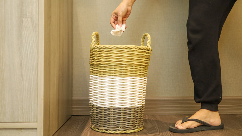 Hand drops crumpled tissue into wicker trash