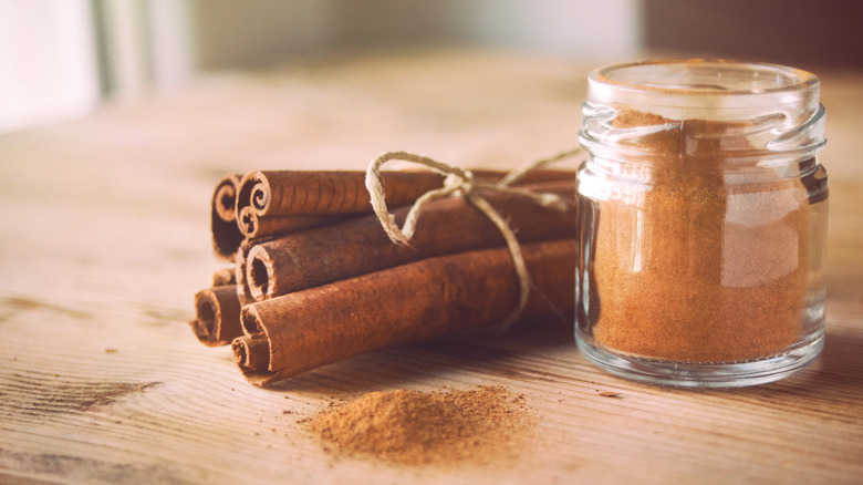 bundle of five cinnamon sticks next to a glass jar of ground cinnamon on a wooden table