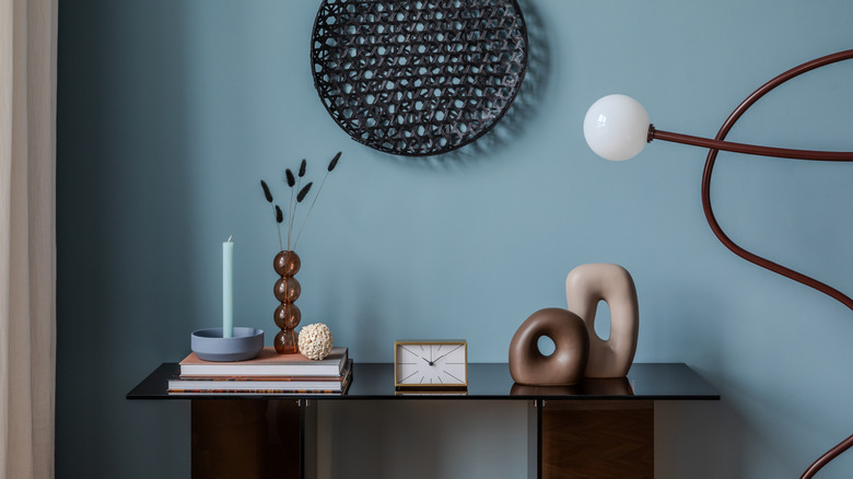 An entryway is painted light blue and features a modern lamp and entryway table.