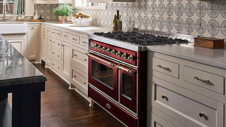 A burgundy range oven in a modern kitchen with white cabinets and a black island.