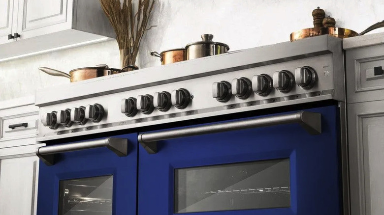A royal blue oven in a kitchen with white cabinets and copper pans on the stovetop.