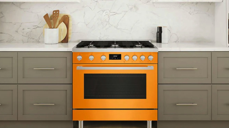 A saffron yellow oven in a kitchen with gray cabinets and a natural stone backsplash.