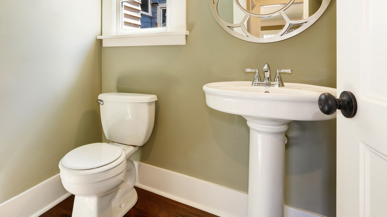 A bathroom with a pedestal sink, toilet, mirror, and window