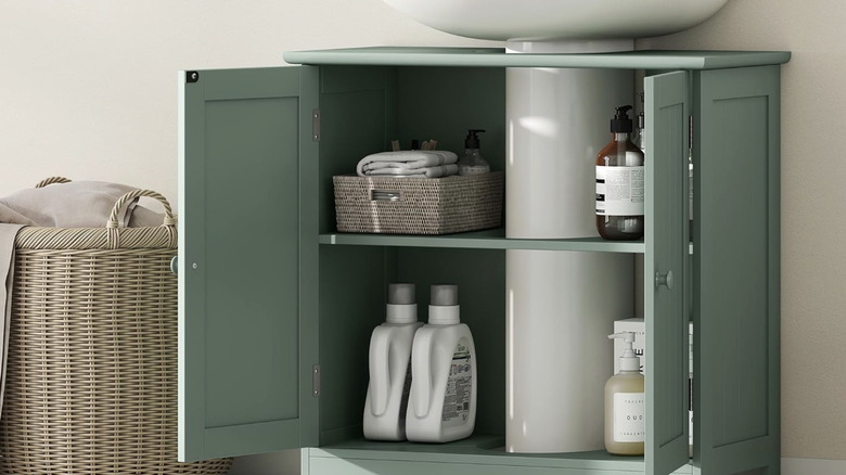 A green bathroom cabinet storing items installed underneath a pedestal sink
