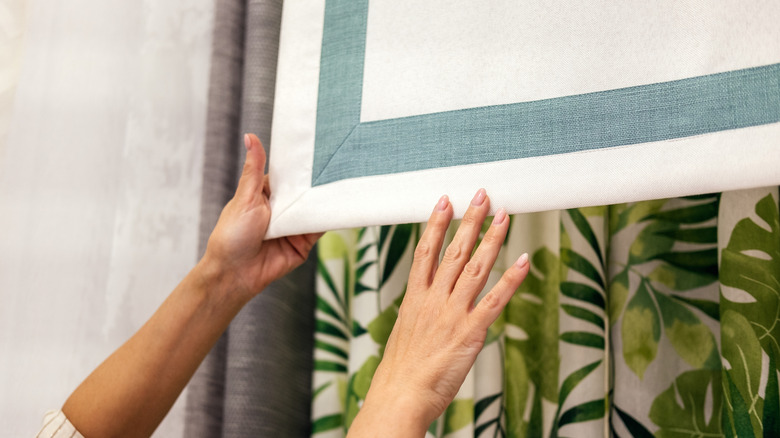 A woman's hands holding white Roman shades trimmed with a green border.