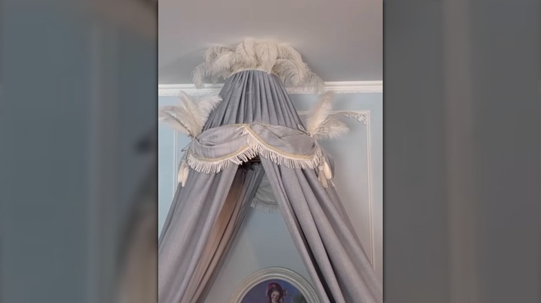 A softly draped DIY bed canopy with feather details made from a thrifted lampshade
