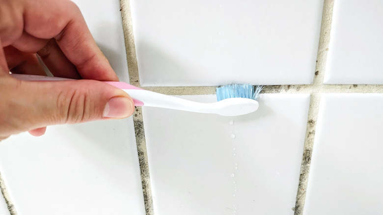 Close up of person using toothbrush to clean tile grout