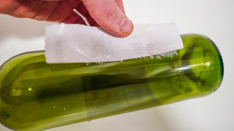 Close up of person removing sticky label from glass bottle