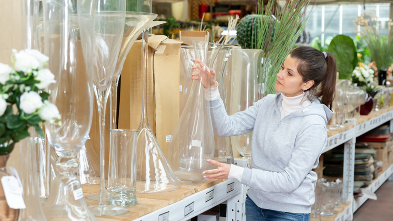 Woman looks at thrifted glass vases, deciding which one she wants to turn into a DIY antique silver makeover.