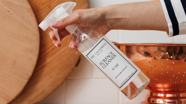 Someone's hand spraying a botttle of The Laundress Surface Cleaner