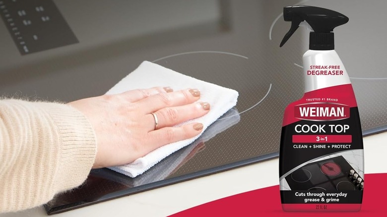 A person using Weiman Daily Cooktop Cleaner on glass cooktop with a bottle of Weiman in the foreground