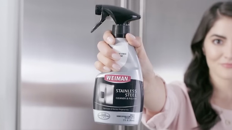 A person holding a bottle of Weiman Stainless Steel Cleaner