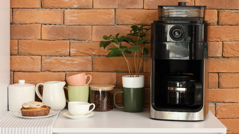 A kitchen counter covered in coffee cups, a coffee maker, and other supplies.