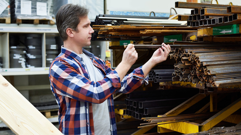 Man examining construction rebar in metal section of hardware store