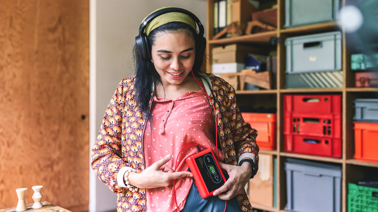A young woman listens to a vintage Walkman with an old-school storage unit behind her.