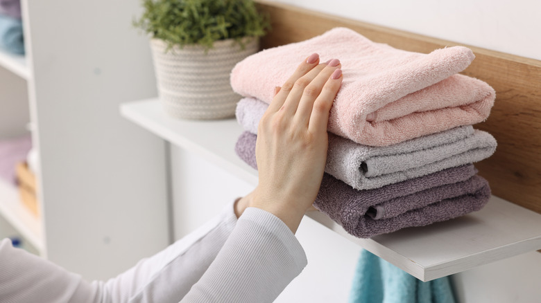 A person placing folded towels on a shelf