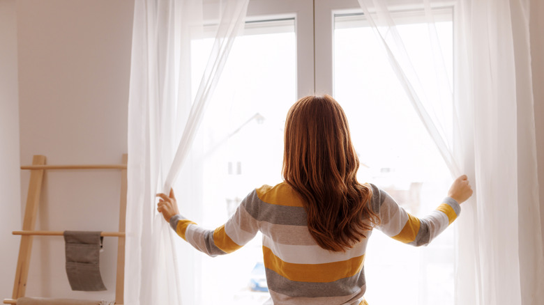 Woman opening sheer curtains from a window