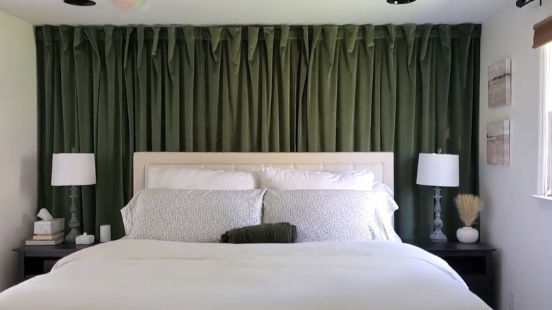 A mostly white bed with a dark green curtain wall behind it