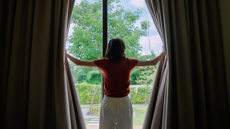 A woman opening up curtains to let in natural light at a sliding glass door