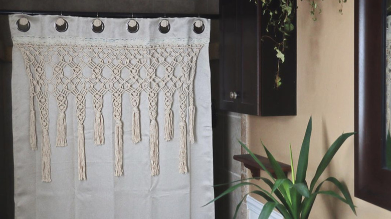 A macrame shower curtain in a neutral, plant-filled bathroom