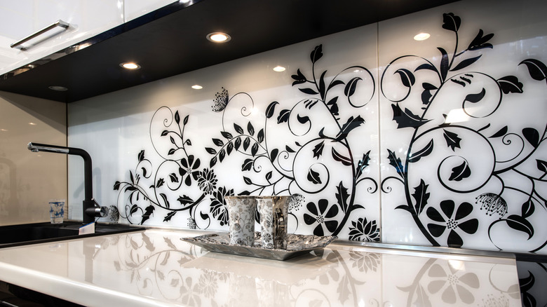 Large backsplash tile with black flowers over white background above kitchen countertop