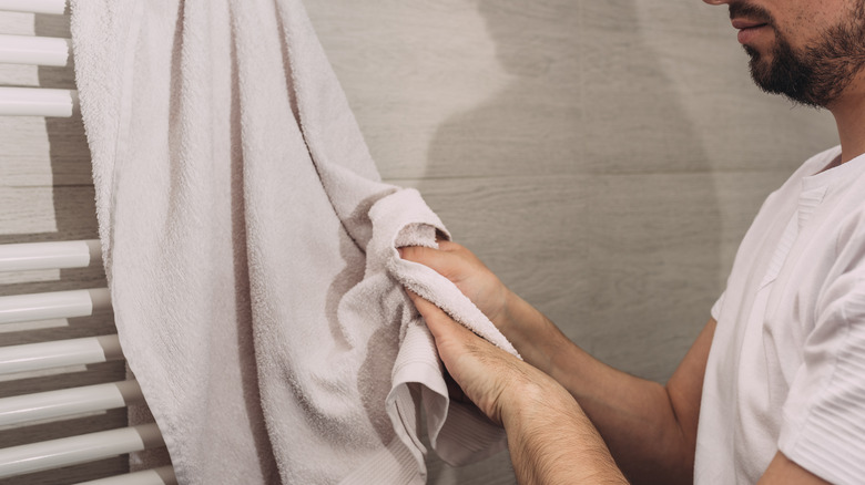 A man dries his hands on a towel hanging on a large wall-mounted towel rack in the bathroom.