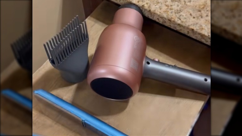 A hair dryer and a straightener sit on a DIY wooden top for an open drawer.