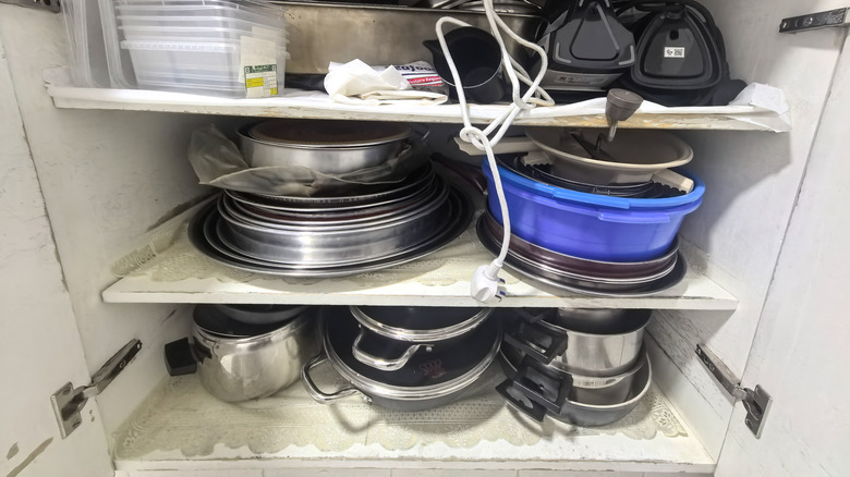 Pot lids poorly stacked in a cupboard
