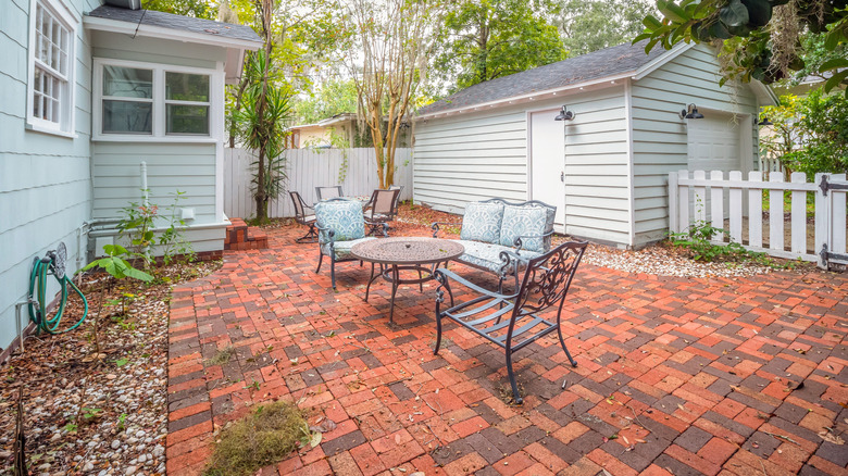 A brick paver patio with metal furniture at the back of a wooden home.