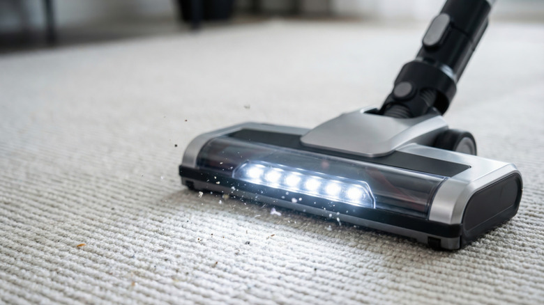 A close up of a vacuum cleaner head with LED lights vacuuming up debris from a cream carpet.