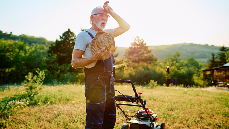 An older man wiping sweat from his forehead after doing lawn work