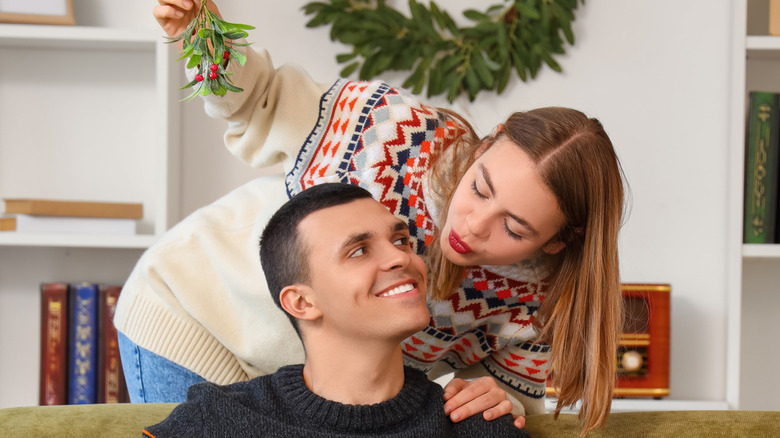 Woman holds mistletoe and puckers, ready to kiss man